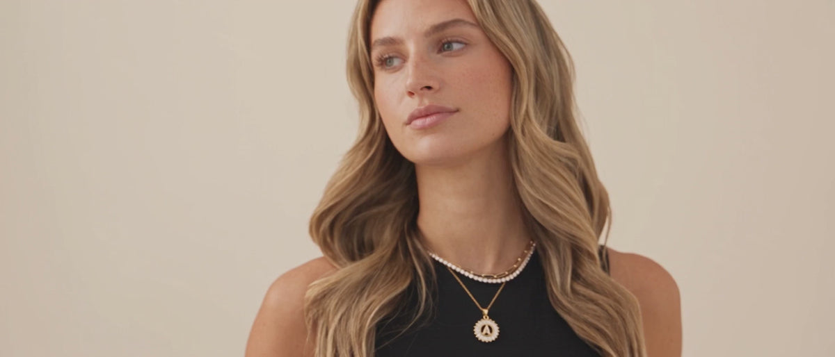 Model in a black top wearing a gold filled CZ tennis choker, oval paperclip necklace and CZ initial pendant layered together