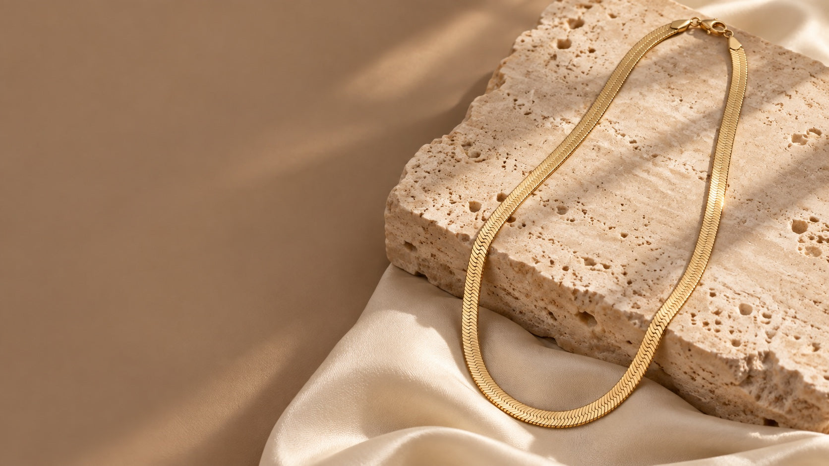 Gold herringbone necklace draped over travertine and ivory silk